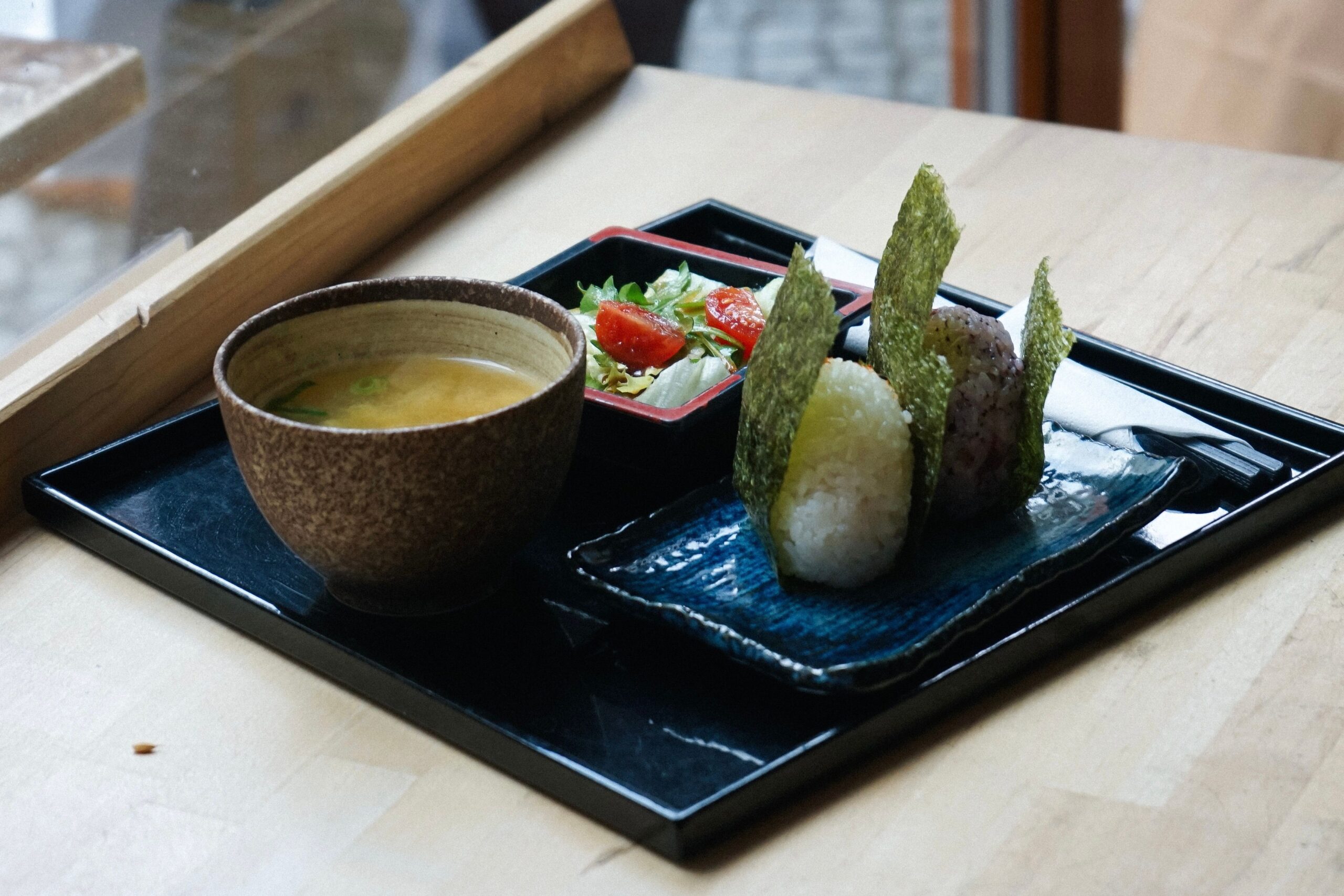 A tray of Japanese miso soup, onigiri rice balls, and salad served in blue ceramic dishes, representing gut-healthy fermented foods